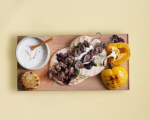 Vildsvinskött på spett på pitabröd. Bredvid grillad paprika och tzatziki